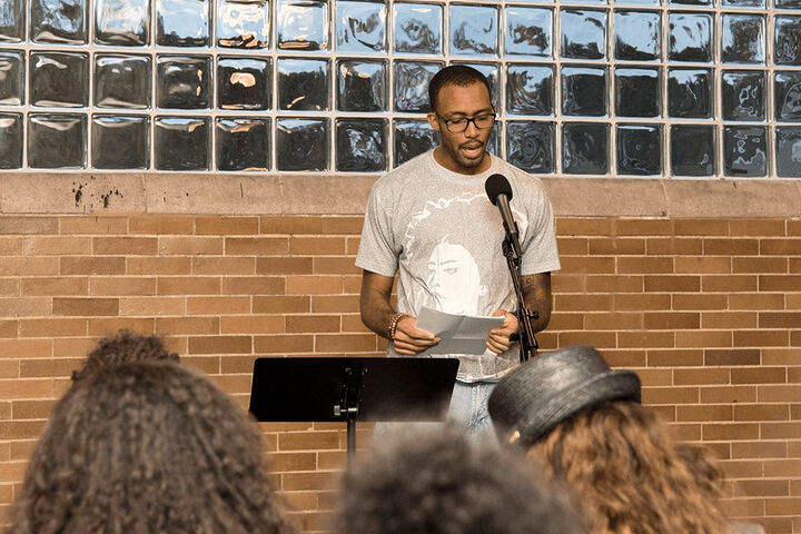 A Black man at the microphone reads in front of an audience at the Civil Rights Heritage Center.